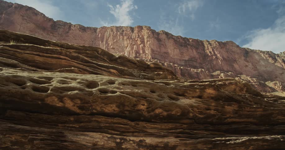 Looking up from river level at the south rim of the Grand Canyon under a blue sky and white wispy clouds from a raft on the Colorado River