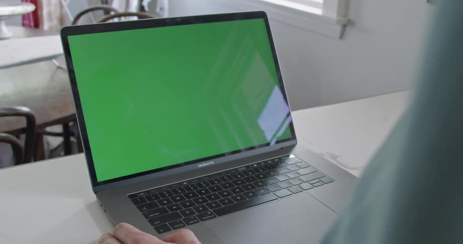 A laptop sits on a kitchen counter with a mans hand on it