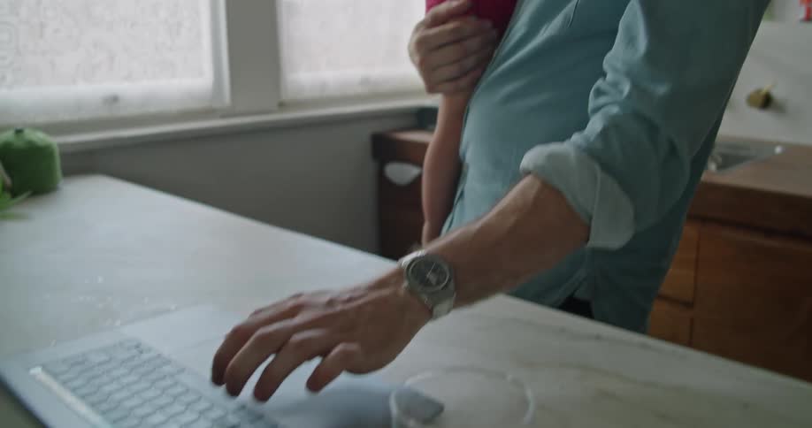 Father holds her daughter and uses laptop in the kitchen
