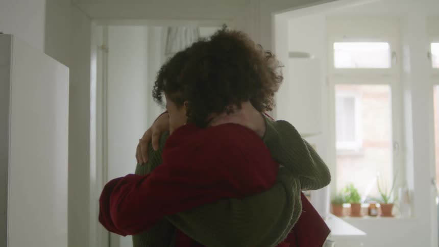 A woman jumps up onto a man and embraces him in a hallway at home during the day
