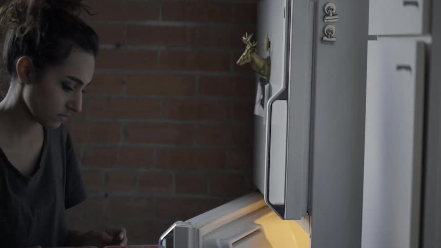 A woman reaches into a refrigerator, pulls out a carton of eggs and closes the refrigerator door