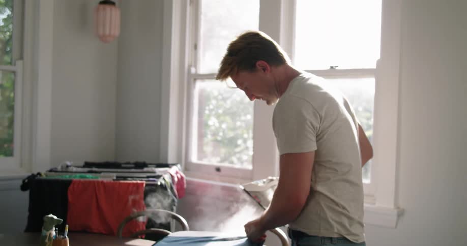 Blonde man with white t shirt and jeans does the ironing