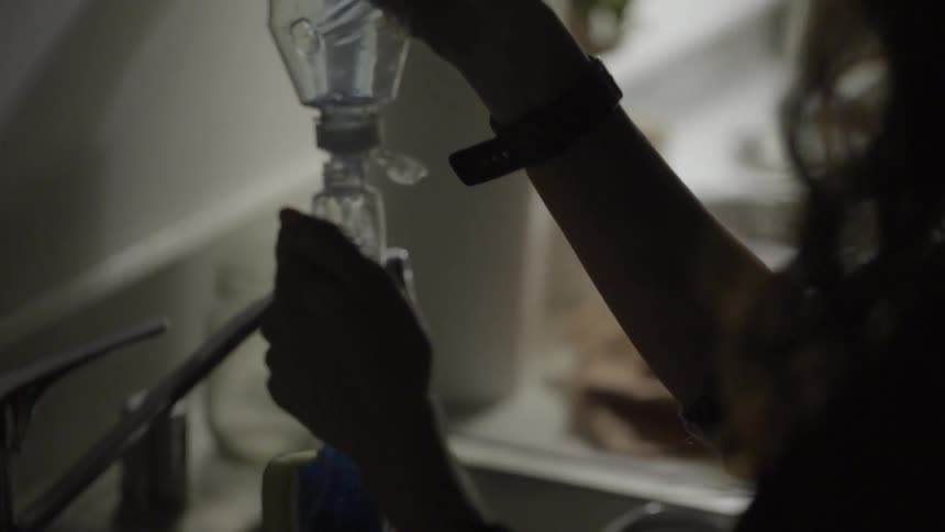 A woman pours dishwashing liquid from one container to another