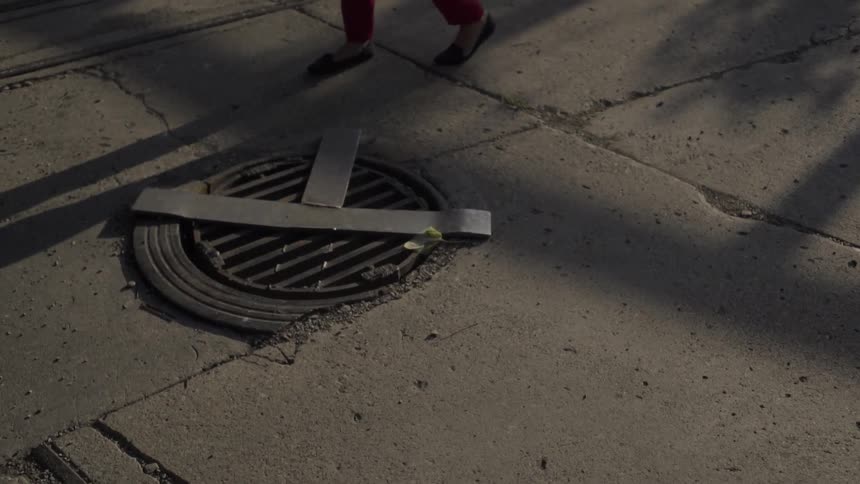 A woman walks by a storm drain and her shadow precedes her on the ground