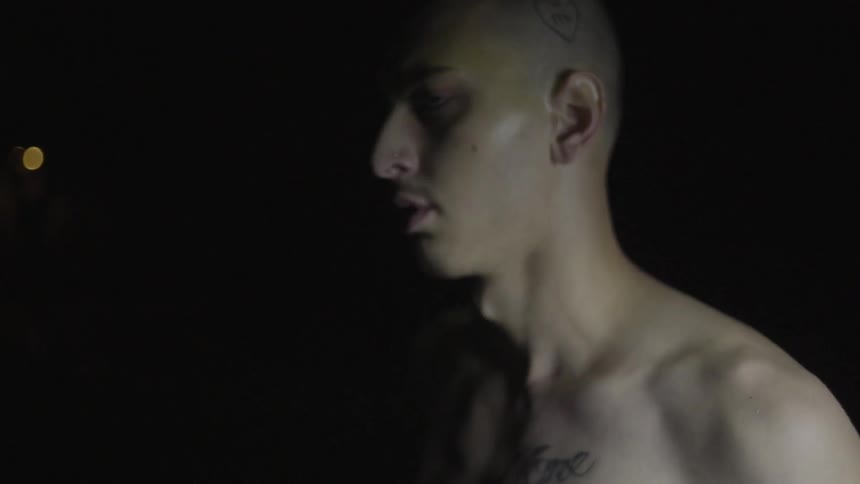 A tattooed man smokes a cigarette outside at night