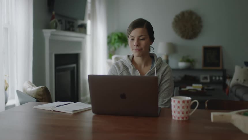 Smiling woman watching something on her laptop on dining table