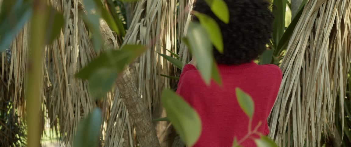 A young woman smiles into the camera while leaning back from a tree trunk