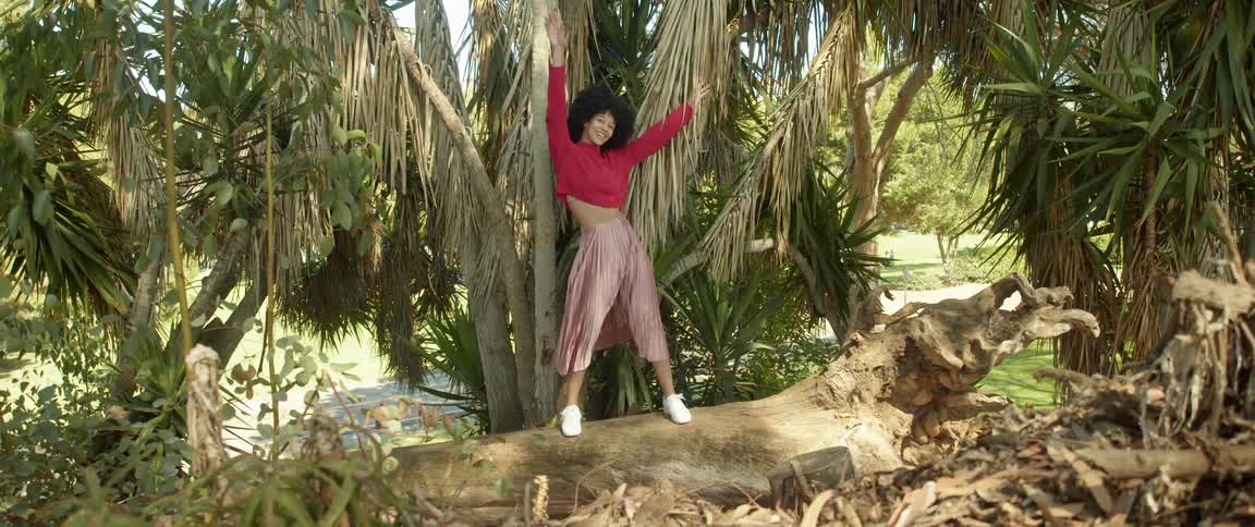 Young woman wearing a long skirt balancing over a fallen tree trunk looking at the camera