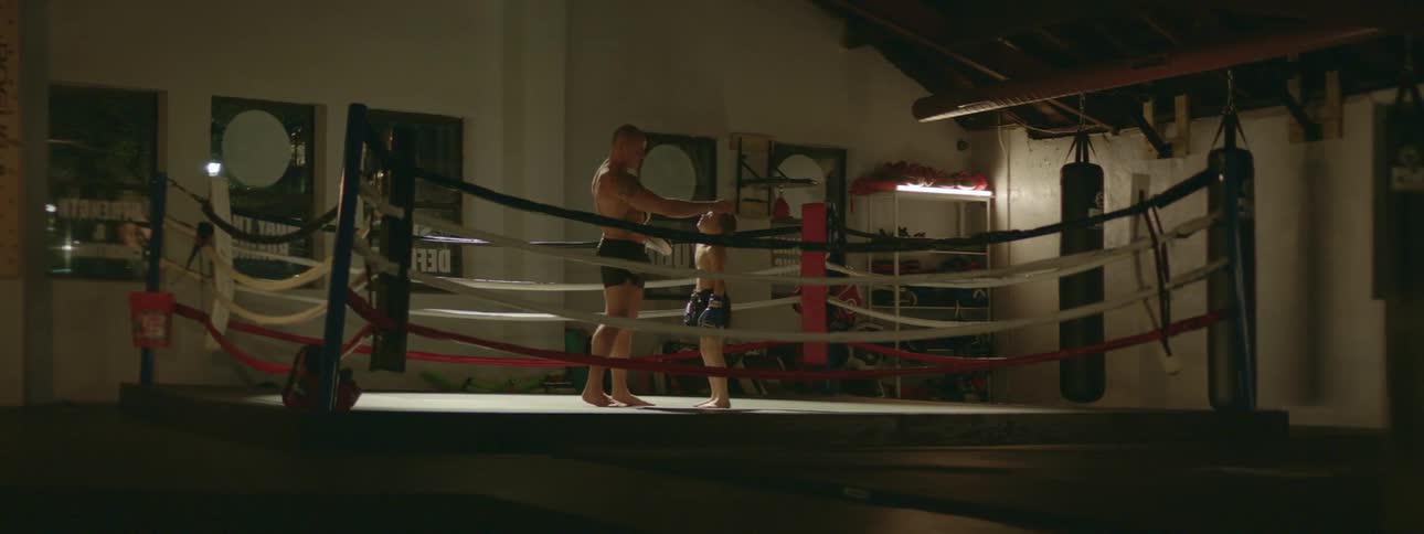 A father pats his son's head in a boxing ring