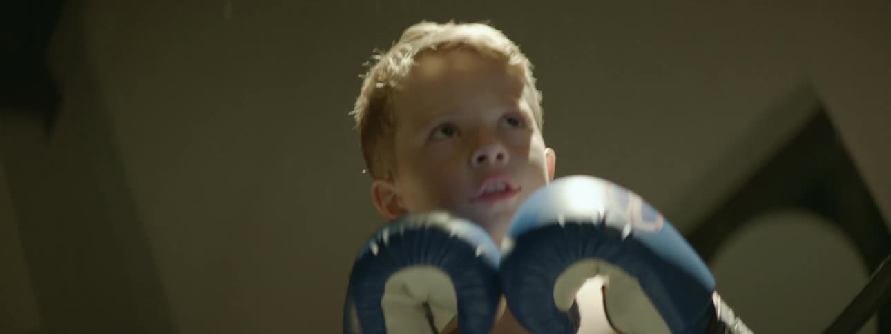 Boy trains in boxing with someone wearing training mitts