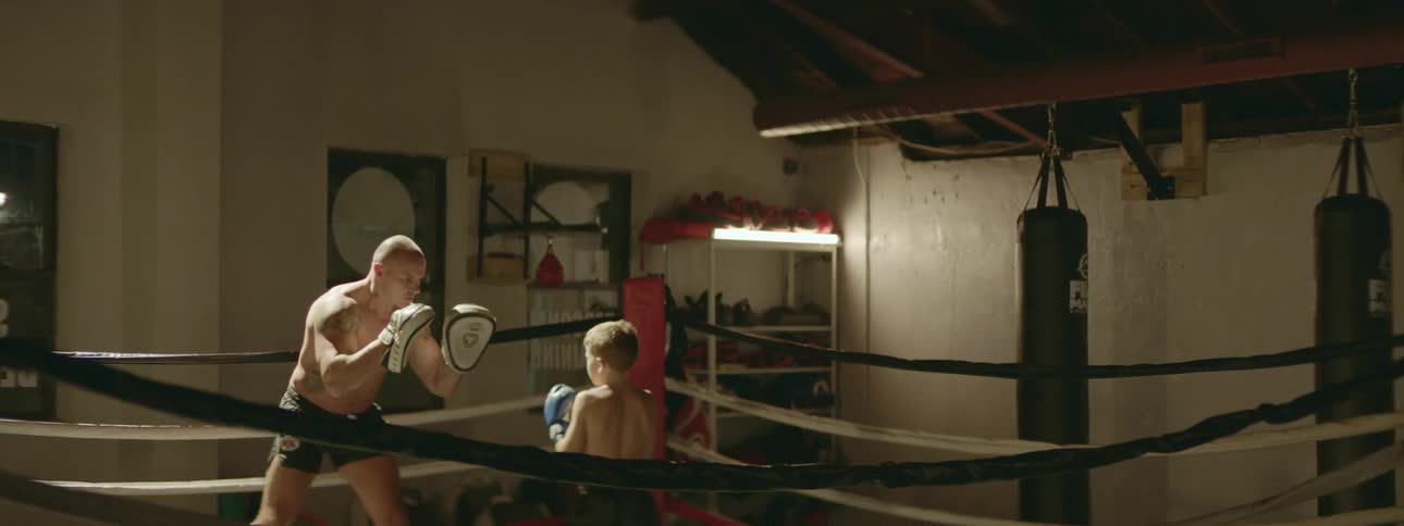 A man coaching a young boy inside a boxing ring