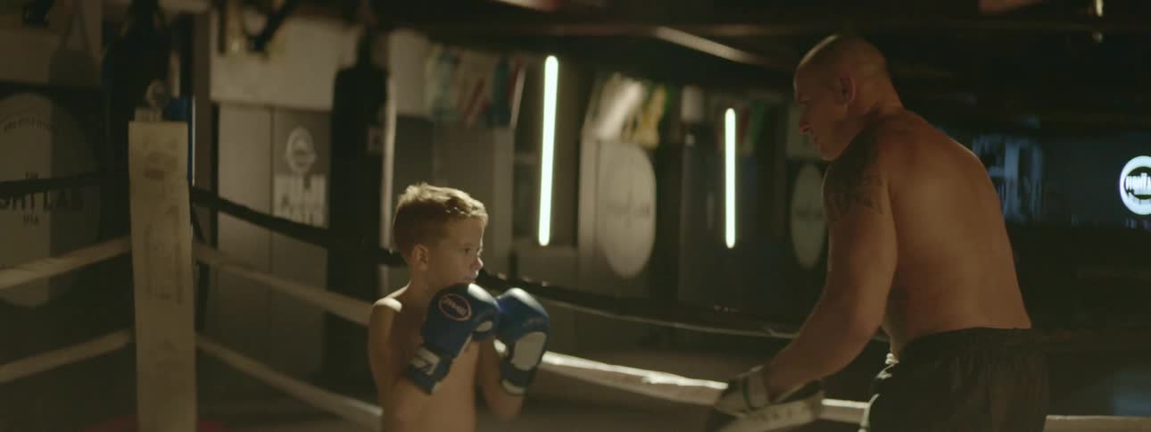 A man coaches a young boy as they box in a ring