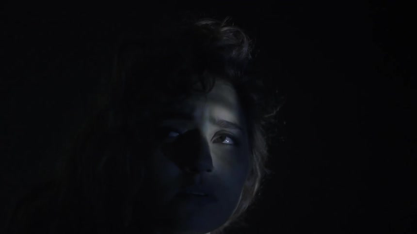 Woman stands in darkness while light flickers across her face