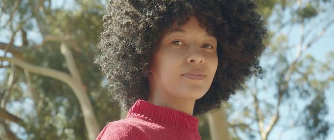 A young woman smiles into the camera while standing outdoors on a sunny day