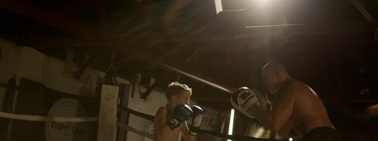 Boy spars with boxing instructor in boxing ring