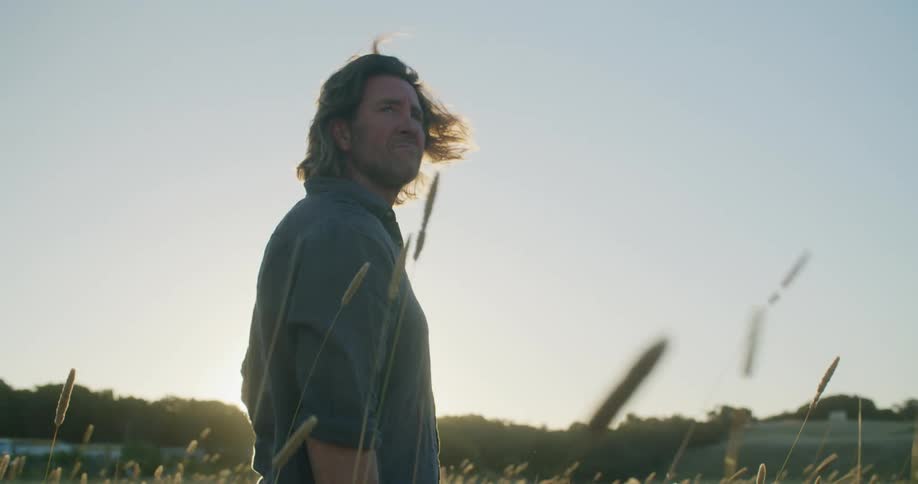 A man stands in a field and looks around as the sun starts to set