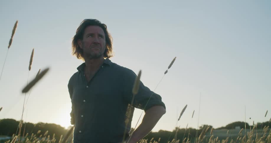 A man standing in a rural grassy field at sunrise