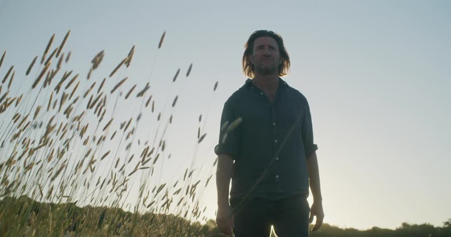 A man walks across a field as the sun sets
