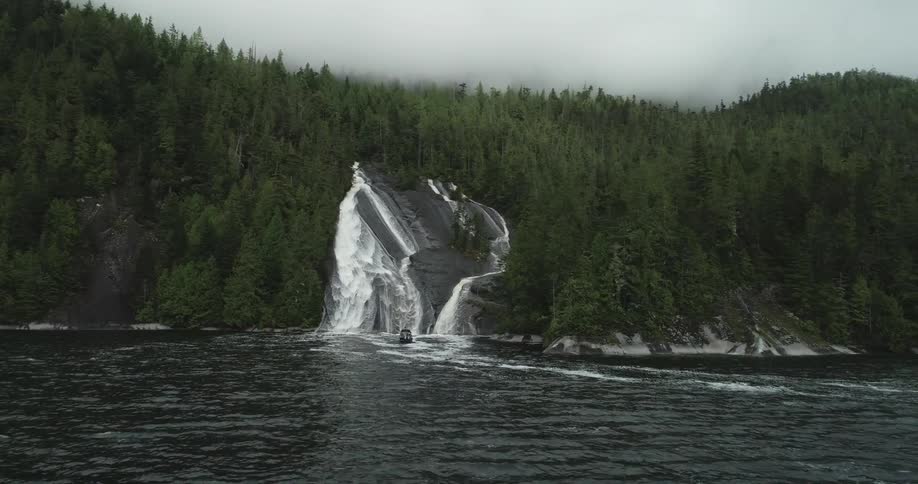 A waterfall moves down the slope of a canyon and into fast moving river water below