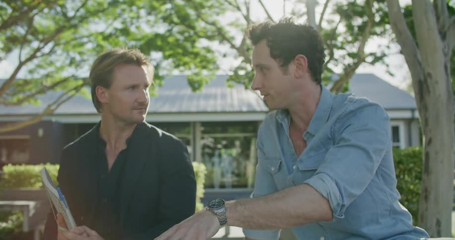 Two men talking outside while referencing a laptop