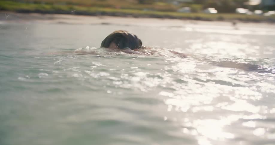 Man swims in ocean with the beach behind him on a sunny day