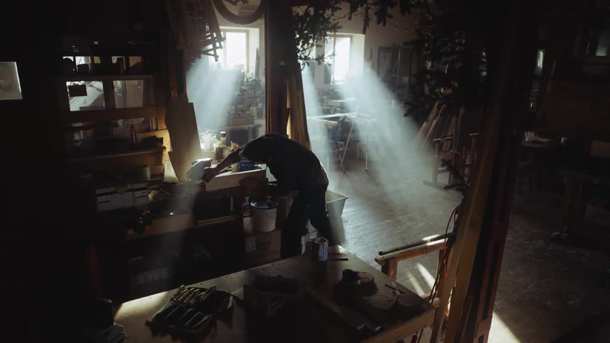 A man sands a piece of wood in his garage filled with woodworking tools