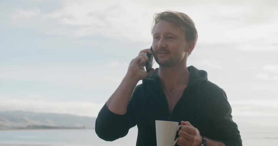 Man talks on mobile phone while drinking coffee on shore