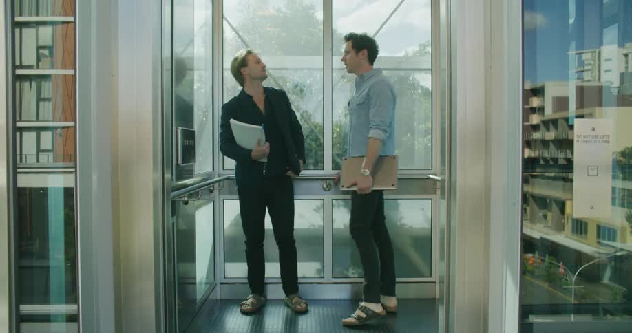 Two men entering a panoramic elevator inside a building