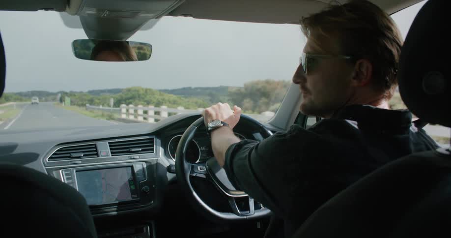 A man with sunglasses driving in a vehicle with the sky and clouds in the background