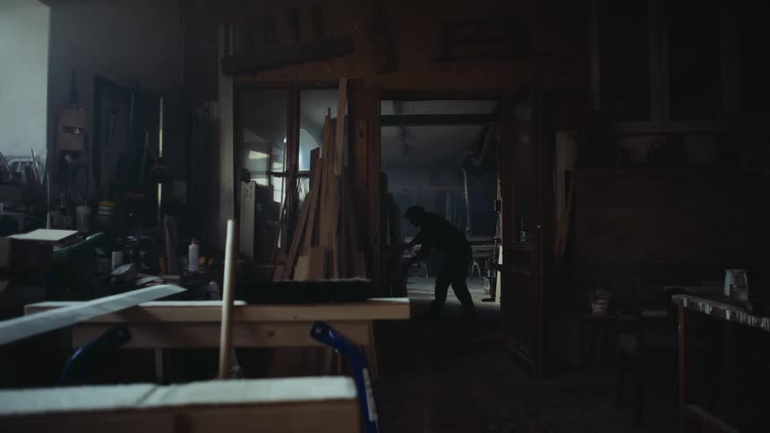 Man works in shadowy woodworking shop