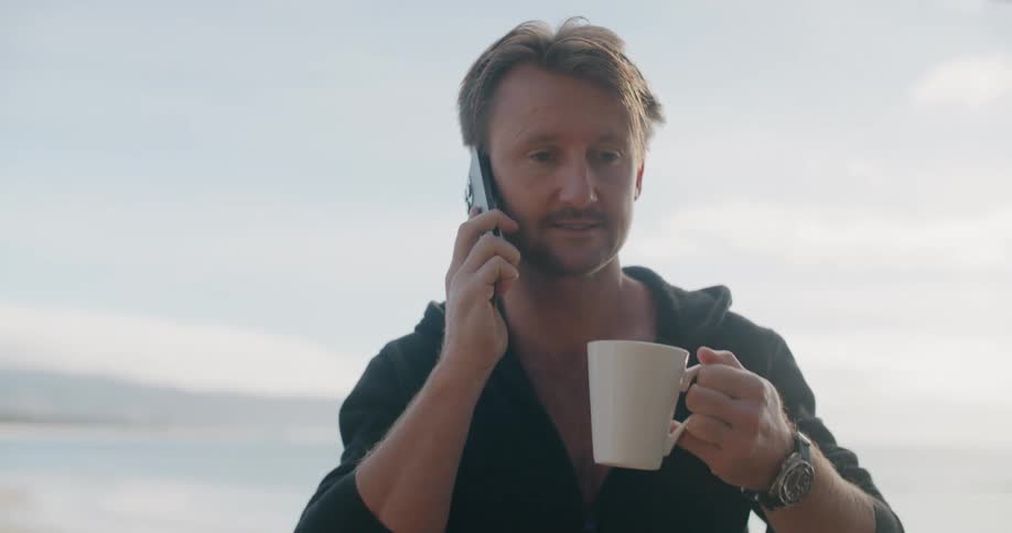 A man talking on a smartphone while drinking coffee outside on a summer day