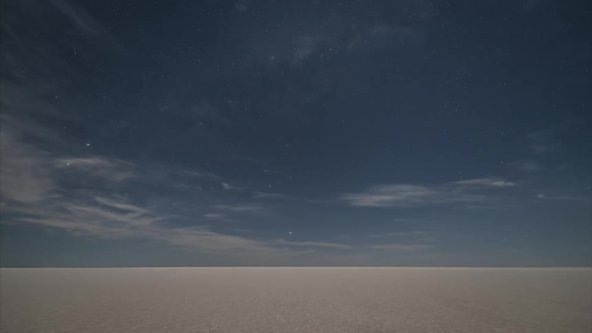Clouds moving over open land with some visible stars in the sky