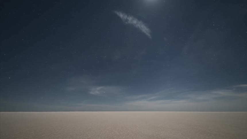 Clouds pass over a vast empty desert at night