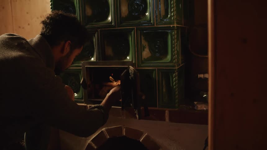 A man lighting an oven with a match on a dimly lit room