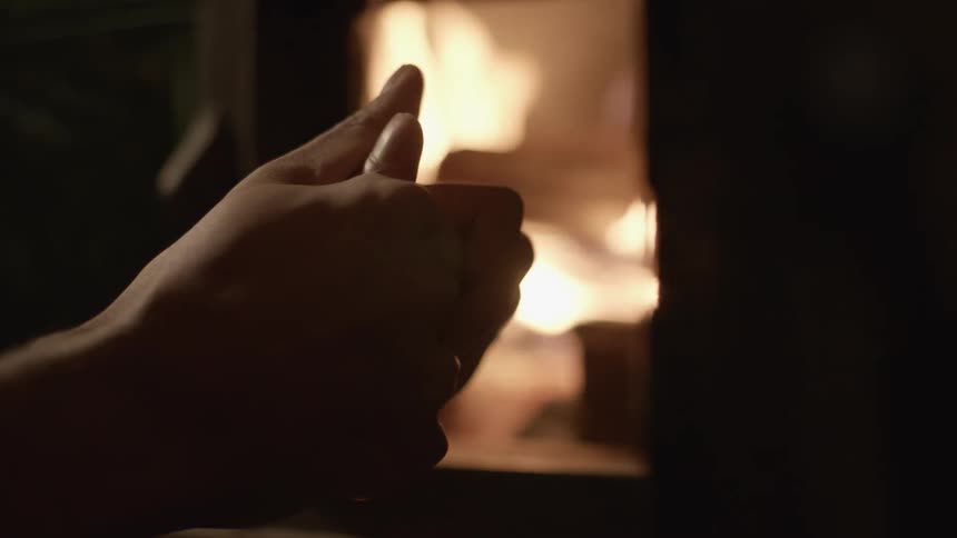 A person warming their hands by a fireplace with fire logs and smoke
