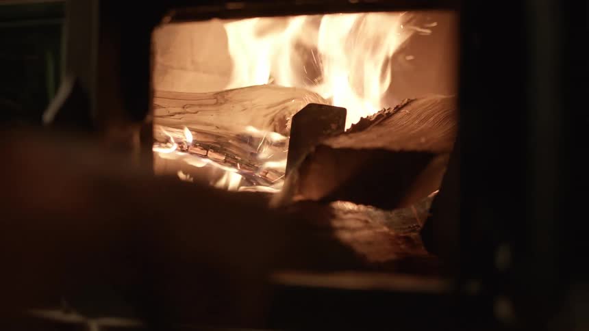 A person puts wood in to a burning fireplace and closes the cover on it