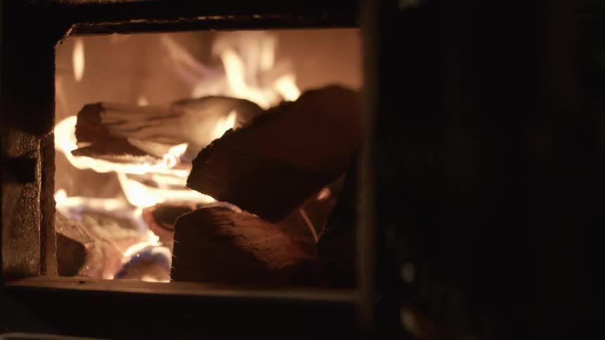 Person places wood on fire in wood burning stove