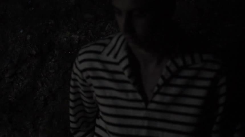 A man in a striped shirt stands next to a wall of rock at night