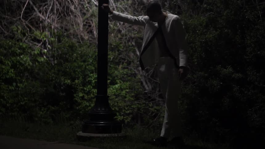 A man leans against a pole in a dark area