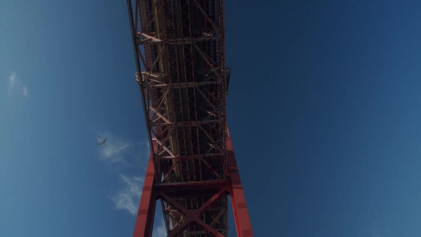 A comercial plane flying on the blue sky over a bridge