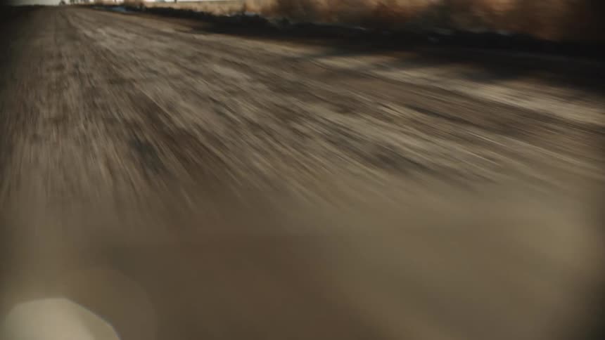 A blue vintage car kicks up dirt as it speeds along a dirt road
