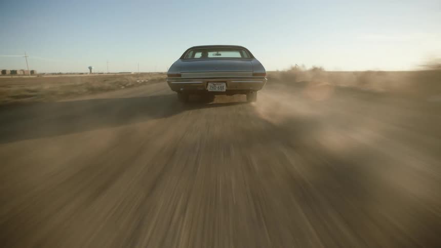 The vehicle is driving on the long dirt road