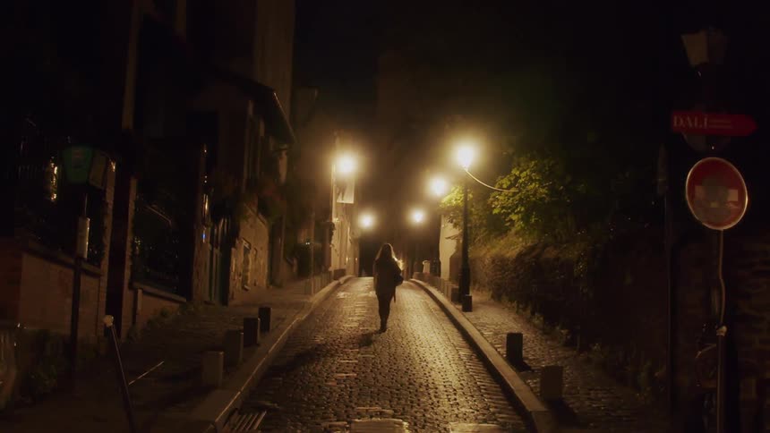 Woman walking on the middle of a cobblestone street in a small town at night