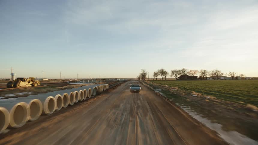 A car driving on a road raising dust with the sky and clouds in the background