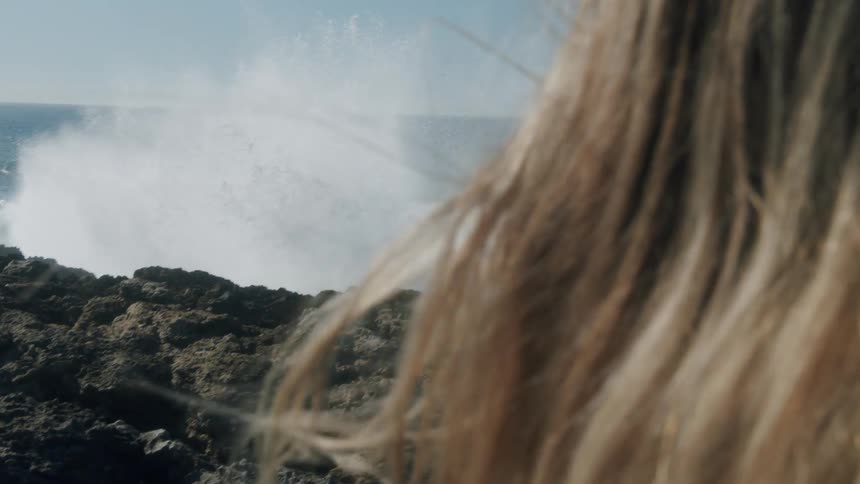 A person standing on a rocky coast with the ocean sky and clouds in the background