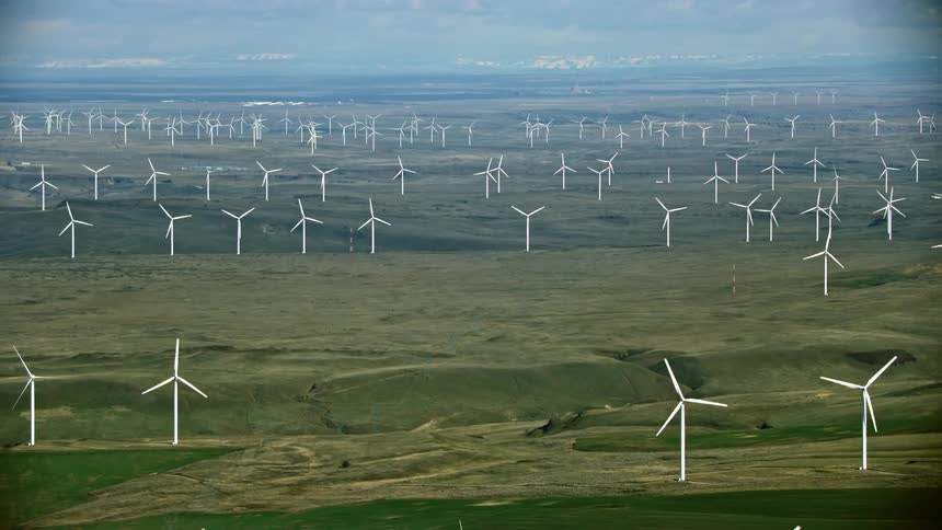 High altitude aerial shot of white wind turbines spinning generating tremendous amounts of renewable energy on a wind farm in western USA
