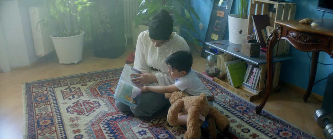 A mother teaches her son a to read with a picture book while sitting on a carpet at home in their living room