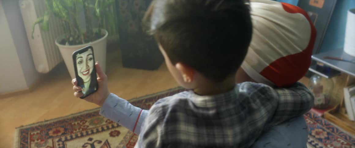A woman uses a smartphone to video chat with another woman before being joined by her young son