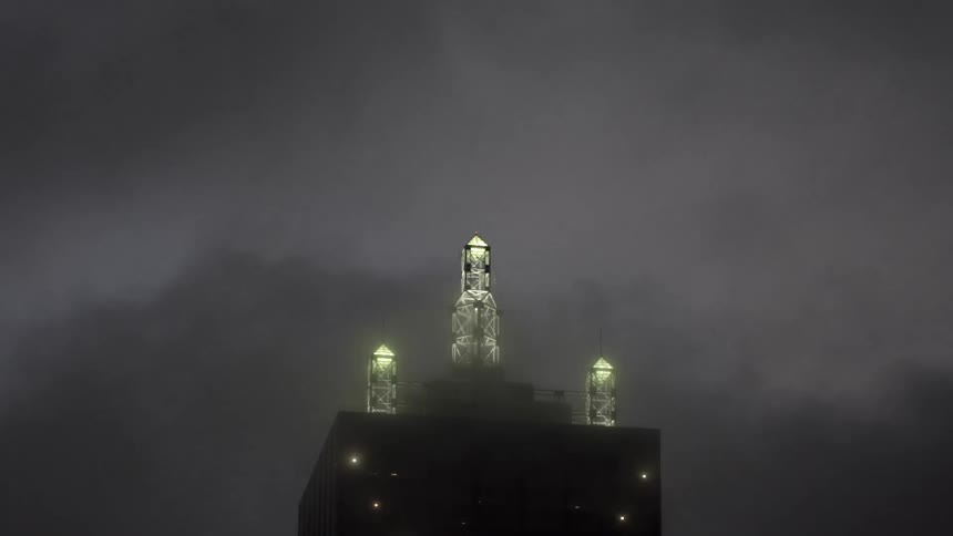 Illuminated pillars on top of a skyscraper as seen through the fog at night