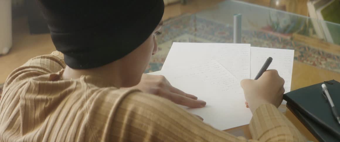 Man wearing a toque writes on a plain piece of paper with a pen